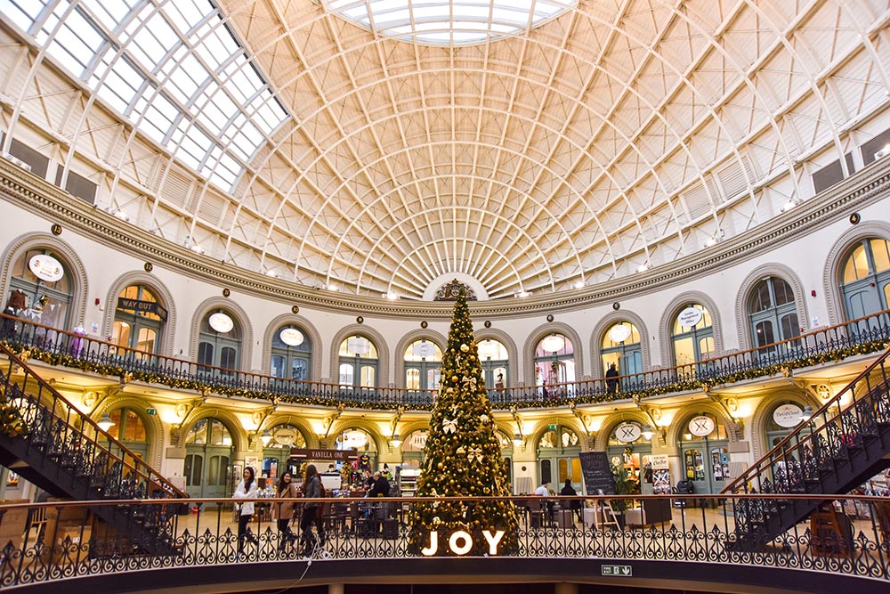 A photograph of Leeds Corn Exchange decorated in Garlands and Lights with a giant Christmas Tree in the middle decorated by Fizzco.l