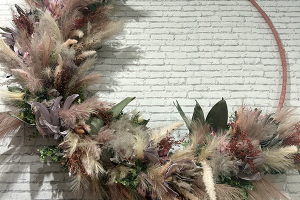 A large hoop with pampas grass and artficial flowers feathered around one half of the design.