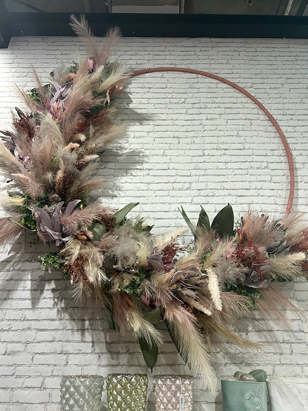 A large hoop with pampas grass and artficial flowers feathered around one half of the design.